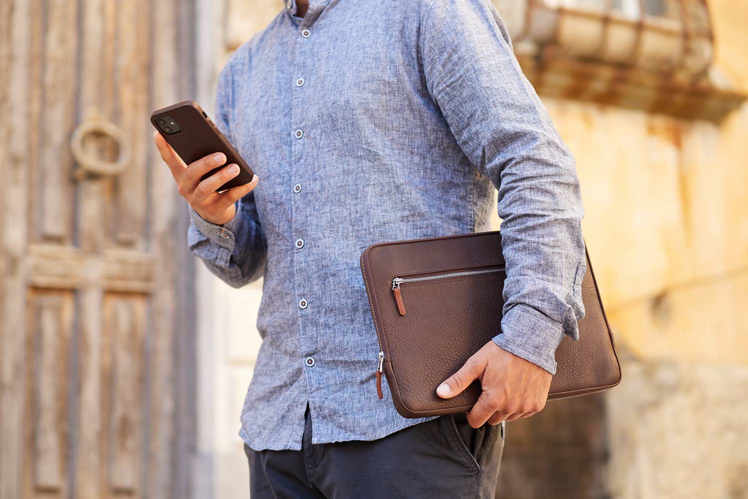 Ein Mann trägt ein Apple Leder Case unter dem Arm und hält ein iPhone in der Hand