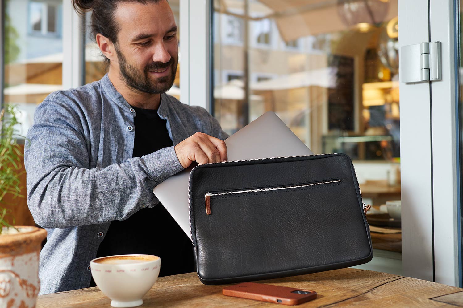 Ein Mann sitz auf einer Bank und steckt sein Laptop in eine Macbook Hülle aus Leder