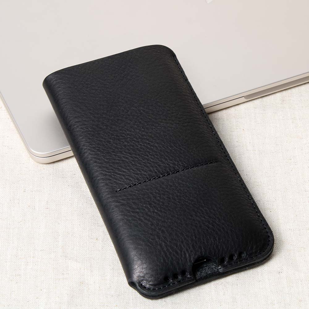 iPhone Sleeve aus hochwertigem Leder mit Ladeaussparung und Soundholes, angelehnt an ein MacBook auf einem Tisch – stilvolle Schutzhülle aus edlem Leder für optimalen Schutz und Funktionalität.