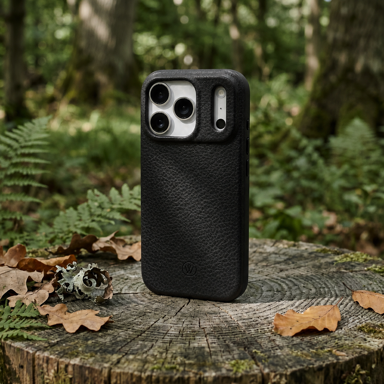 iPhone 17 Pro Hülle aus schwarzem Leder und mit TPU Schutzrahmen steht im Wald auf einem Holzstumpf