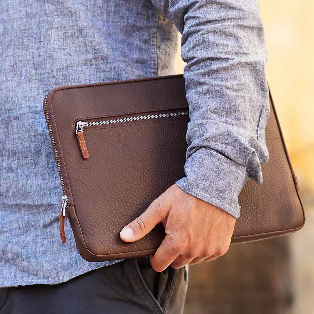 Macbook Tasche aus dunkel braunem Leder wird unter dem Arm getragen