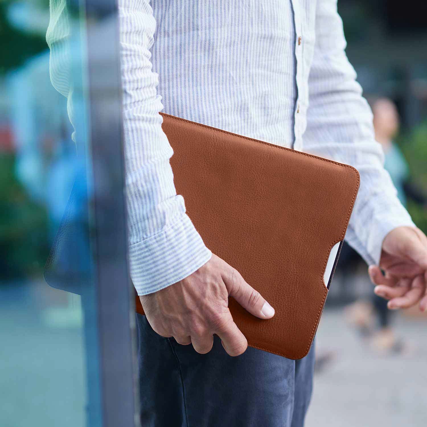 Ein Mann hält in seiner rechten Hand eine Macbook Hülle von GoodWilhelm unter dem Arm